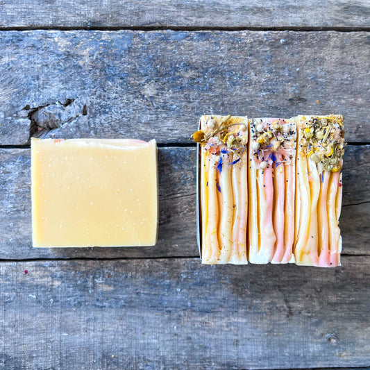 Bar of soap on a wooden surface with a box of soap bars featuring floral designs.