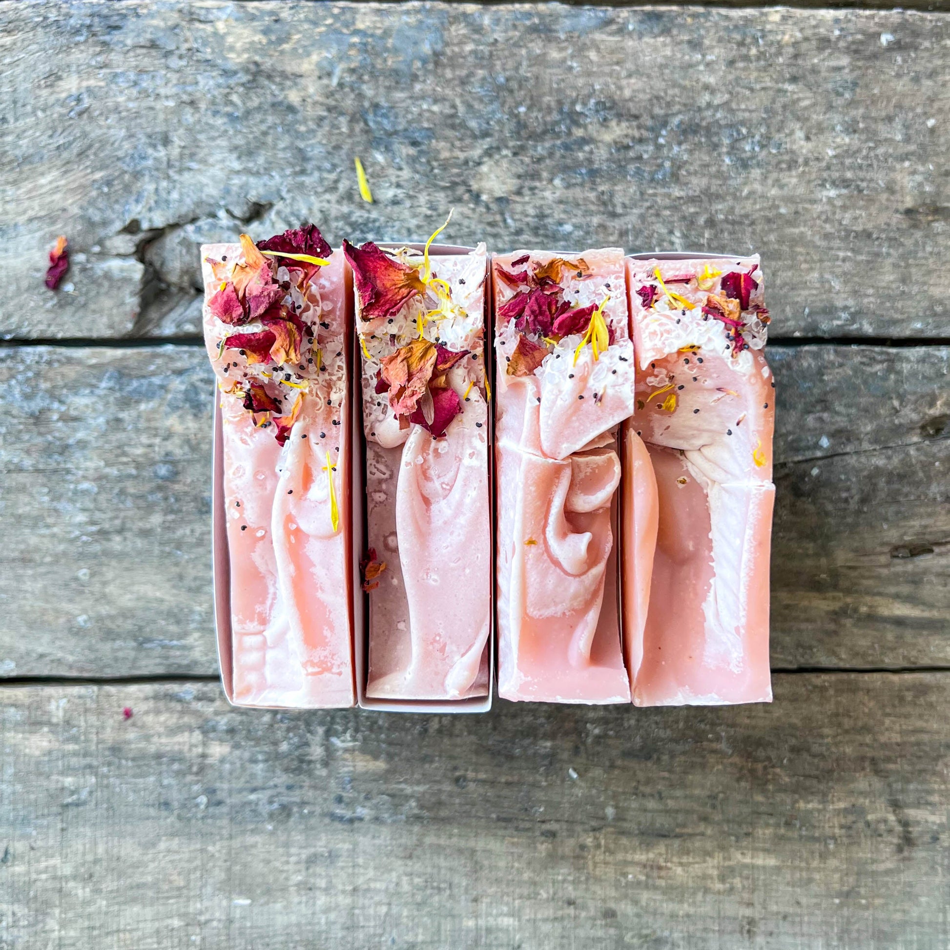 Three pink soap bars with rose petals on a wooden surface
