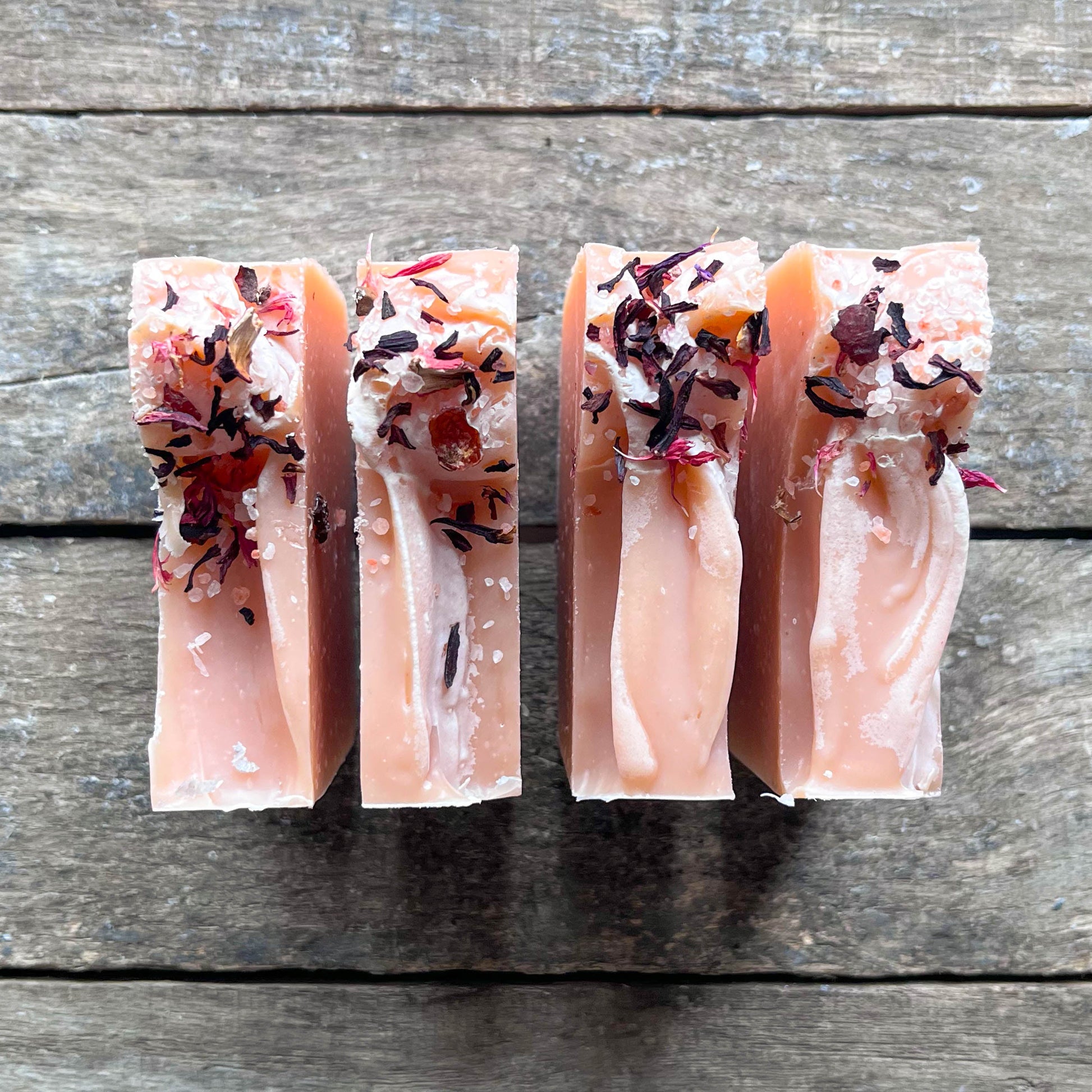 Four rectangular soap bars with floral toppings on a wooden surface